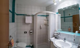 A modern bathroom with a shower, a sink, and a toilet. The walls are tiled and there are some towels and toiletries.