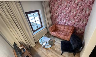 A stylish room with an orange sofa and a black chair. The room has a high window front and a striking, patterned wall.