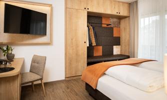A modern room with wood paneling and a large television. There is a comfortable bed, a seating area, and an open wardrobe.