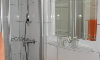 A modern bathroom with a shower and a sink. Towels in striking orange are neatly arranged.