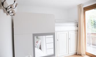 A cozy room with a white loft bed and a wardrobe. The light streams through the window and the walls are bright and kept simple.