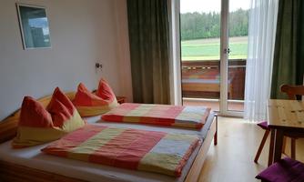 A cozy room with two beds and colorful cushions. There is access to the balcony with a view of the green landscape.