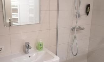 A modern bathroom with a shower and sink. The walls are tiled in light colors and there is a mirror above the sink.