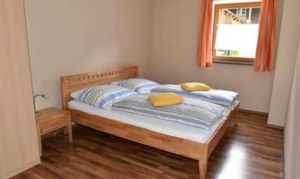 A simple bedroom with a double bed and two pillows. The room is bright and cheerful with a window that lets in daylight.