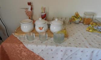 A table with various dishes, including two white pots and several glasses. Additionally, some utensils and a decorative hen can be seen.