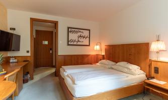 A modern hotel room with a double bed and wood paneling. There is a television, nightstands, and warm light from the lamps.