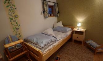 A cozy children's room with a single bed, a bedside lamp, and a小 chair. The walls are adorned with decorative wallpaper and a colorful mural.