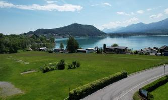 A wide meadow overlooking a clear lake and gentle hills in the background. The landscape is green and sunny, ideal for relaxation and enjoyment of nature.