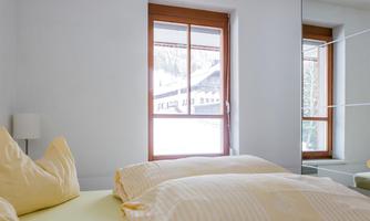 A bright bedroom with a large window and a view of snow-covered mountains. The beds are cozy and equipped with yellow pillows.