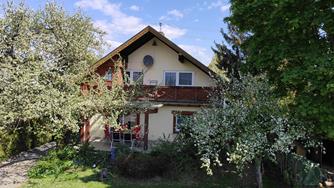 A beautiful house surrounded by blossoming trees and a green garden. The sky is blue with some clouds.