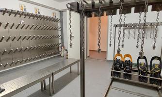 A room with stainless steel hooks and a bench, ideal for storing ski equipment. In the foreground are ski boots, and various holders hang on the wall.