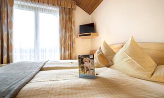 A cozy bedroom with two beds and a large window. On the bed lies a book that indicates the relaxed atmosphere.