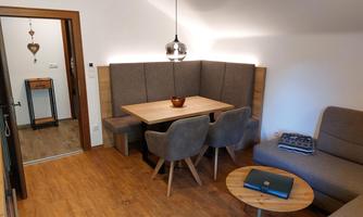 A cozy living space with a wooden dining area and comfortable chairs. A bowl is on the table and in the background, a gray sofa can be seen.