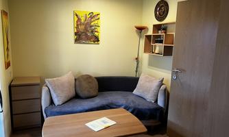 A small room with a blue sofa and a wooden table. On the wall hangs a piece of artwork and a clock.
