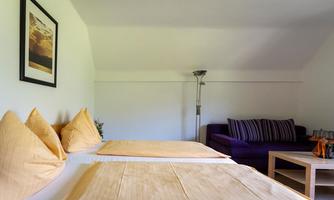 A bright room with two beds and orange bedspreads. In the background, there is a purple couch and a table.