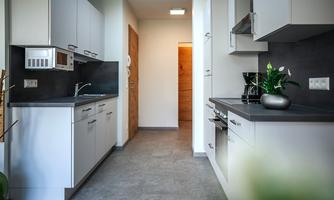A modern kitchen with bright cabinets and a gray countertop. The rooms are bright and well-lit, with a view of an entrance door.