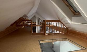 A cozy attic with wooden details and a modern glass floor. The slope of the roof creates an interesting atmosphere.