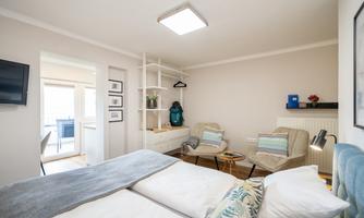 A modern room with two beds, comfortable armchairs, and a television on the wall. There is a small table and a pleasant atmosphere.