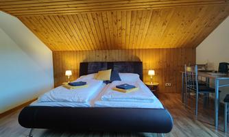 A cozy bedroom with two beds and wooden paneled walls. There is a small table and chairs as well as soft lighting.