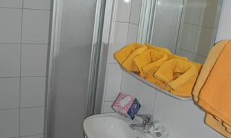 A modern bathroom with a shower, a sink, and a large mirror. Yellow towels are on the shelf and a trash can is also visible.
