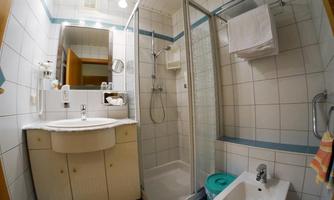 A small bathroom with a shower, sink, and toilet. The walls are tiled, and there are towels and toiletries visible.