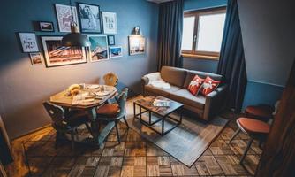 A cozy living space with a table, chairs, and a couch. Pictures are hanging on the wall, and the window lets in plenty of light.