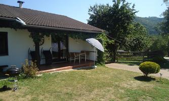 A cozy house with a covered seating area and garden furniture. The garden is green and inviting, surrounded by trees and a grassy area.