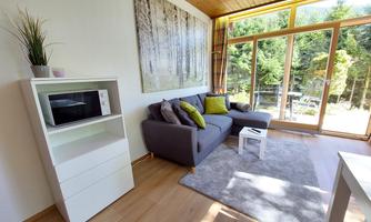 A modern living room with a gray sofa and colorful cushions. Large windows offer a view of the garden.