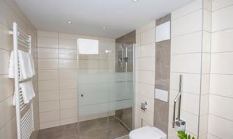 A modern bathroom with a walk-in shower and bright tile design. Towels are neatly hung, and the decor feels clean and inviting.