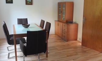 A cozy dining area with a wooden table and six black chairs. In the background, there is a modern wooden sideboard next to a door.