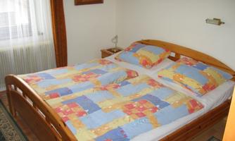 A cozy bedroom with a wooden bed and colorful bedspreads. The room has a bright atmosphere due to the window and the curtains.