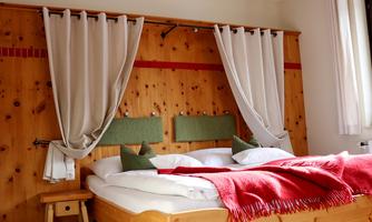 A cozy bedroom with a double bed and wood paneling. The decoration includes gray curtains and a red plaid.