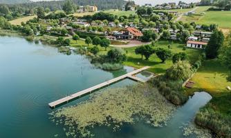 A picturesque lake surrounded by lush greenery and beautiful houses. A pier leads into the water and invites relaxation.