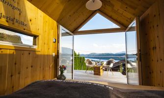 A cozy wooden cottage with a view of the lake. The covered terrace features two chairs and plenty of daylight.