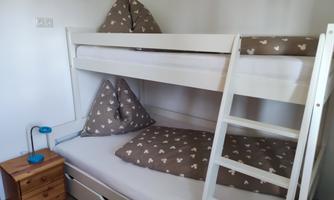 A room with a bunk bed and cozy cushions. Next to the bed is a nightstand with a lamp.