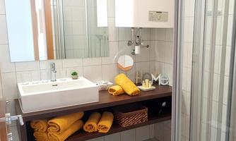 A bright bathroom with a modern sink and a mirror. Towels in yellow are neatly folded and placed on a shelf.