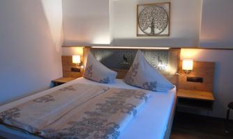 A cozy bedroom with a large bed and decorative pillows. A calm atmosphere is created by the soft lighting and the wall mural.