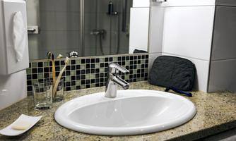 A modern sink on a granite base with brushes, a glass, and a towel. In the background, a shower is visible.
