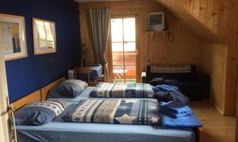 A cozy bedroom with two beds and blue bedding. There is a window overlooking a balcony and a seating area.