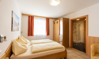 A bright room with two single beds and a modern bathroom. The walls are in neutral colors, and large windows provide plenty of daylight.