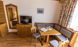 A cozy room with a wooden table and chairs. There is a television, a mirror, and large windows with curtains.