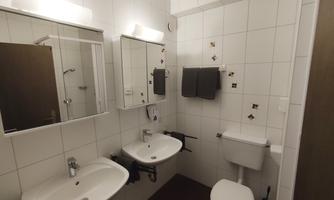 A modern bathroom with white tiles and mirrors. It includes sinks, a toilet, and towels.
