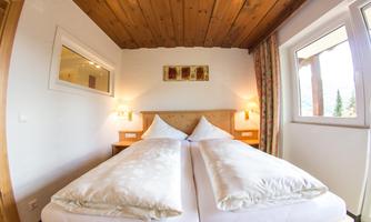 A cozy bedroom with two beds and decorative pillows. The room has wooden ceilings and large windows that let in plenty of light.