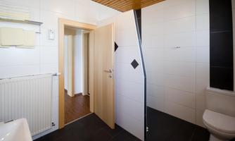 A modern bathroom with white tiles and wooden ceilings. The shower is open, and the room has a bright, inviting atmosphere.