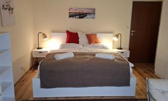 Spacious bedroom with a double bed and seating area (pull-out couch) and ample closet storage and shelves.  
Balcony with a view into the greenery to the west with afternoon sun.
