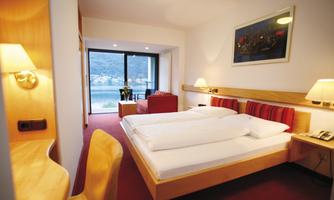 A modern hotel room with a double bed and a cozy seating area. The large windows offer a beautiful view of the surroundings.