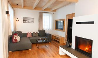 A cozy living room with a modern sofa and a fireplace. Large windows provide plenty of daylight and a pleasant atmosphere.