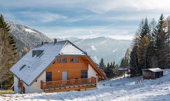 A beautiful, modern house in the mountains, surrounded by snow and pine trees. Majestic mountains with a clear sky can be seen in the background.