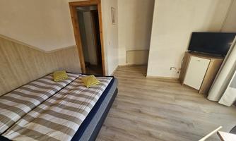 A cozy bedroom with a double bed and a television. The room has bright walls and a wooden floor.