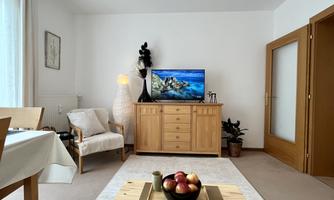 A cozy living room with a wooden piece of furniture and a television. A bowl of apples sits on the table, and the walls are painted light.